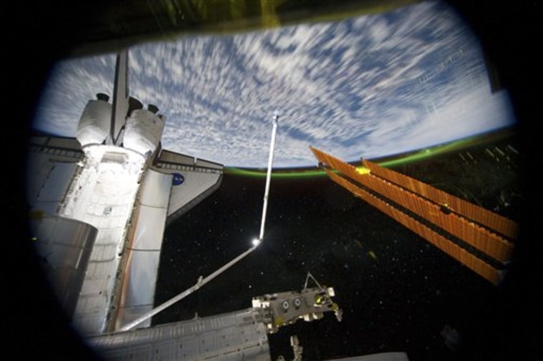 This panoramic view provided by NASA was photographed from the International Space Station, looking past the docked space shuttle Atlantis' cargo bay and part of the station including a solar array panel toward Earth, was taken on July 14, 2011 as the joint complex passed over the southern hemisphere. Aurora Australis or the Southern Lights can be seen on Earth's horizon and a number of stars are visible also. 